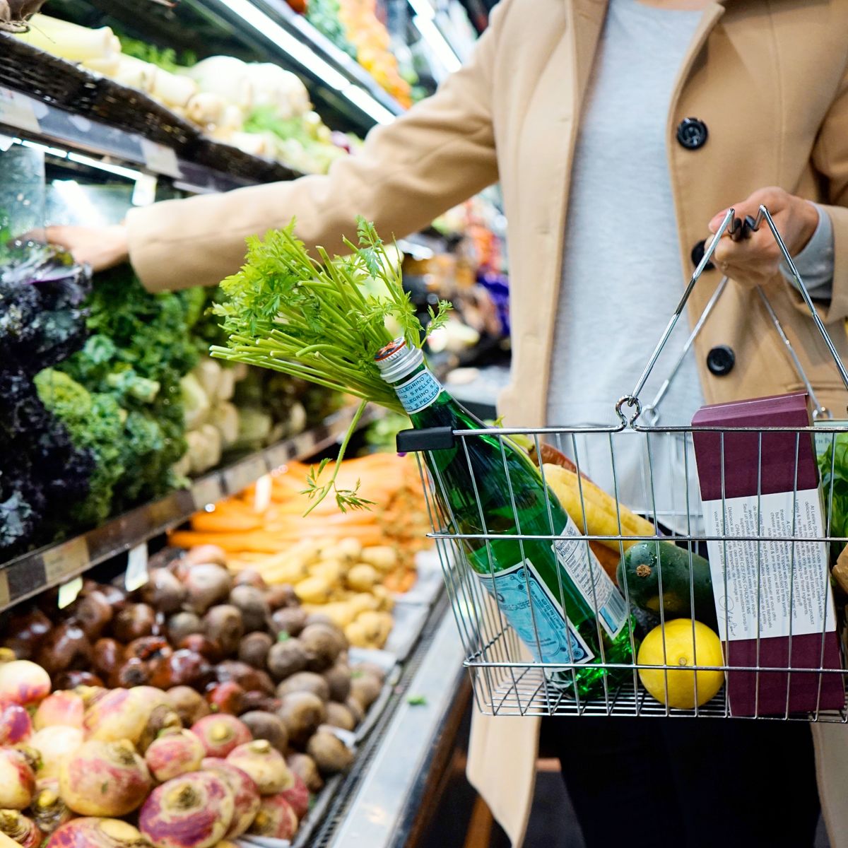 Woman choosing fresh produce at a supermarket with a basket of groceries