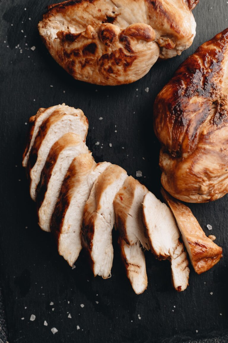 Sliced roasted chicken breasts on a dark surface, a high protein meal.