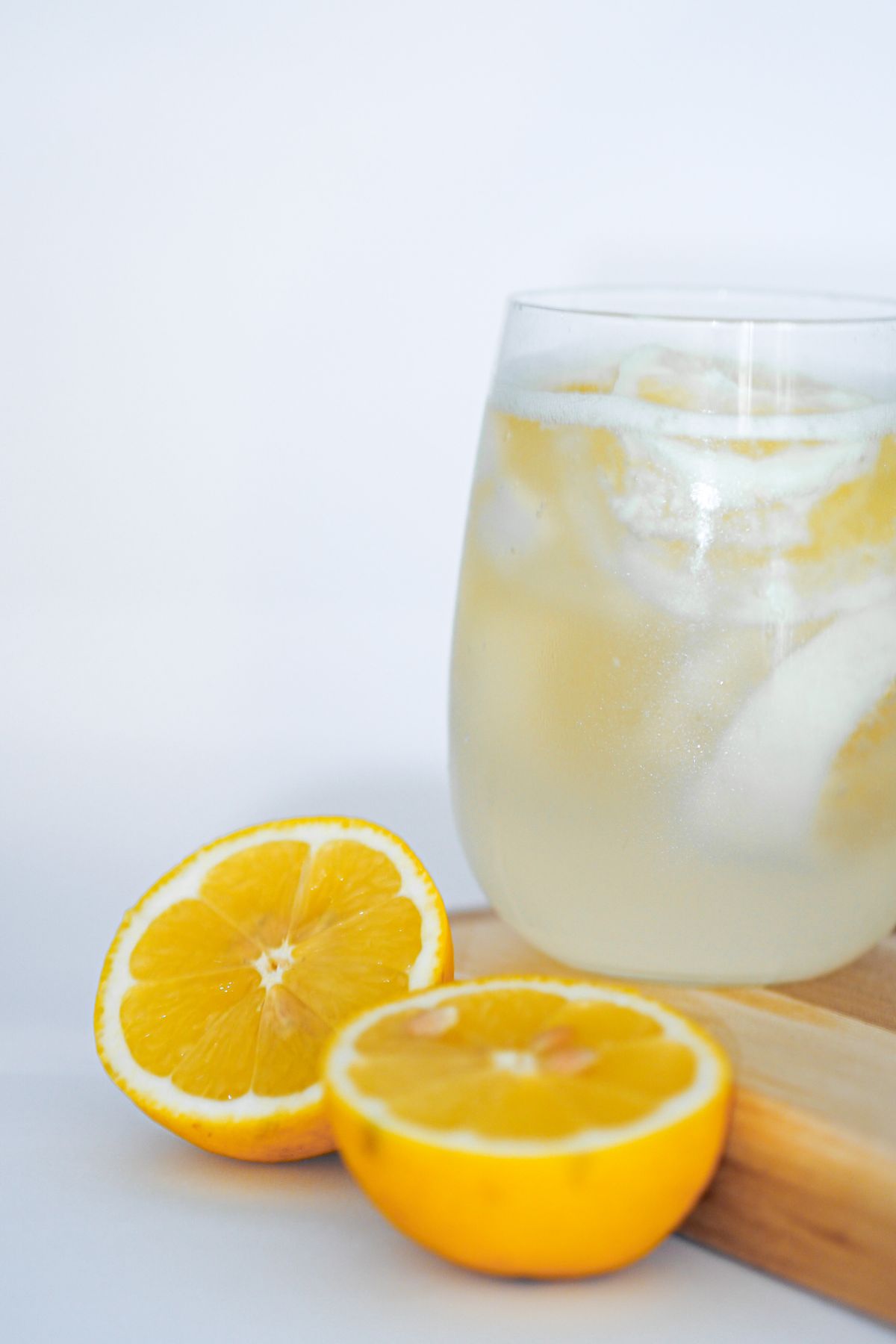 Glass of iced lemon water next to two halved lemons on a cutting board