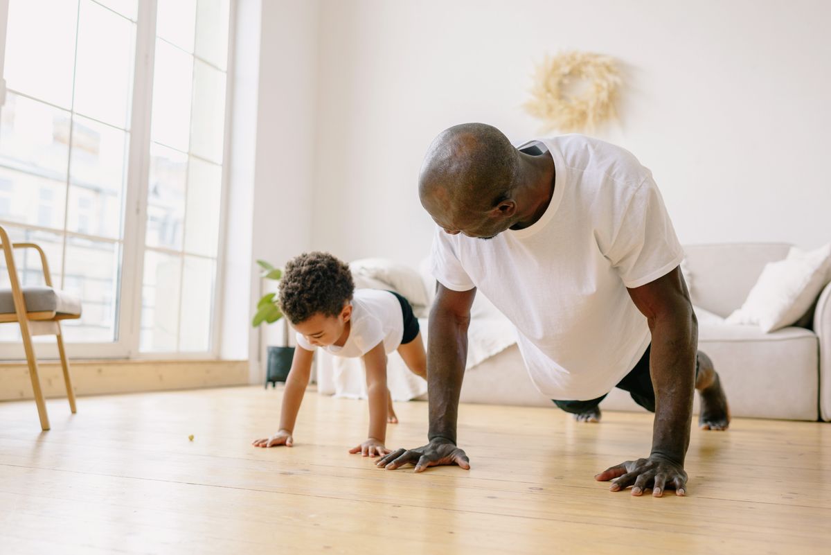 Man and young son doing push-ups together on a wooden floor at home