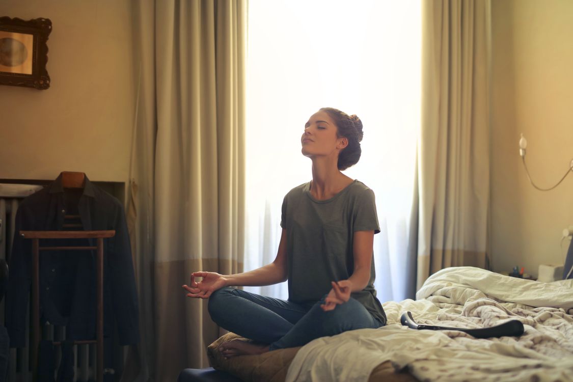 Person sitting on the edge of a bed in soft light practicing slow breathing to relax before sleep