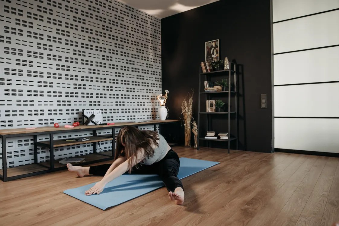 Woman doing a pilates mat workout at home on a mat in a bright living room