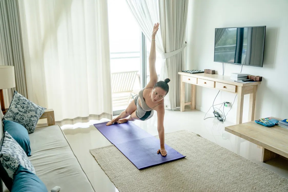 Woman doing a side plank on a mat in a bright living room